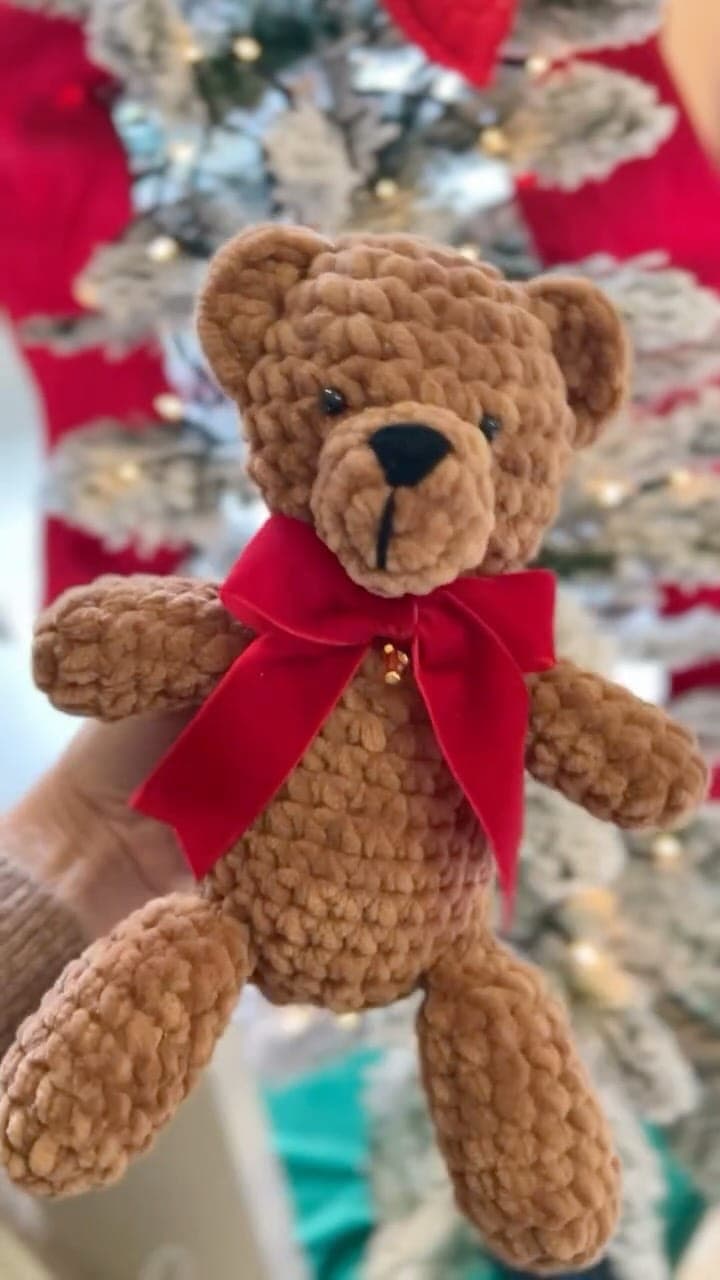 Soft amigurumi teddy bear with a big red bow by the Christmas tree