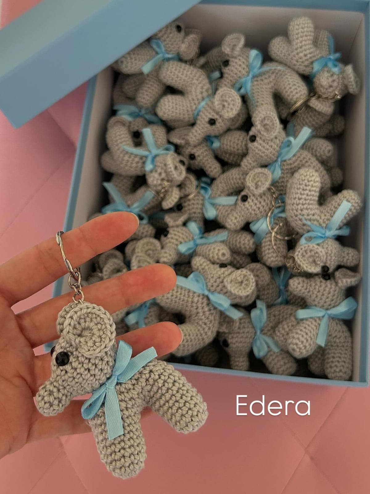 Amigurumi baby elephant keychain with a blue ribbon, from a box full of elephants